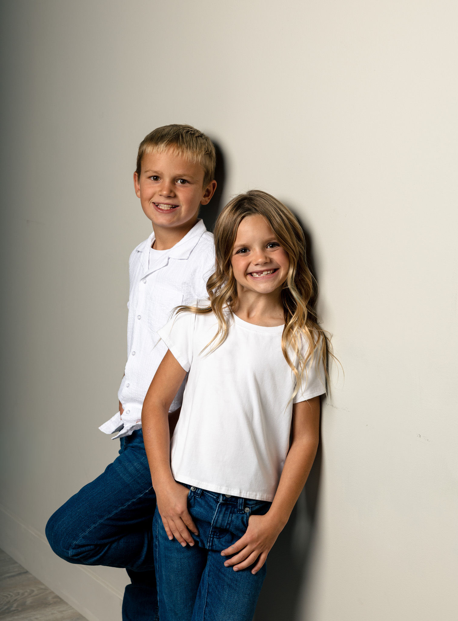 Two kids leaning on white wall.