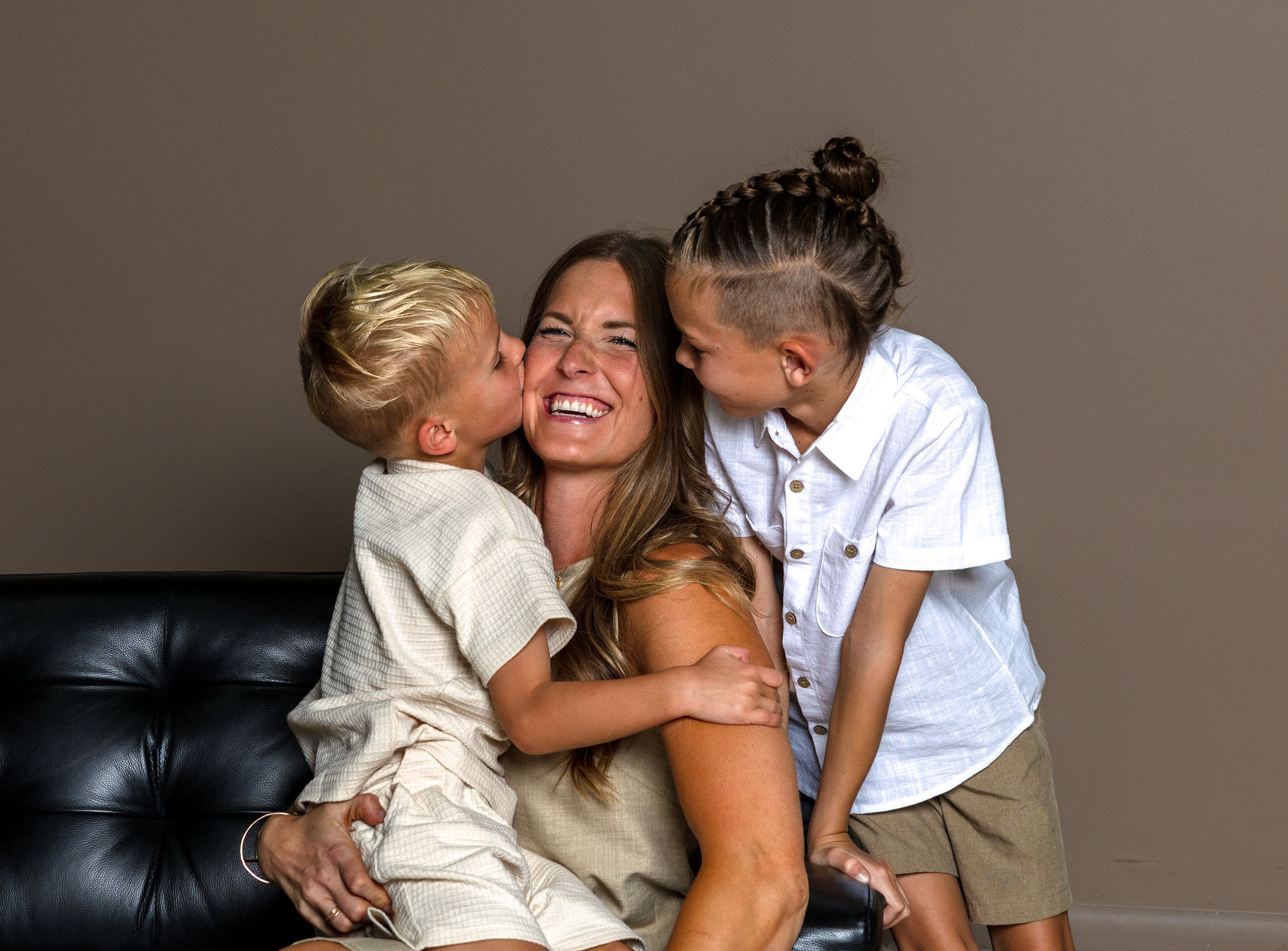 Mom being kissed by her two boys on brown.