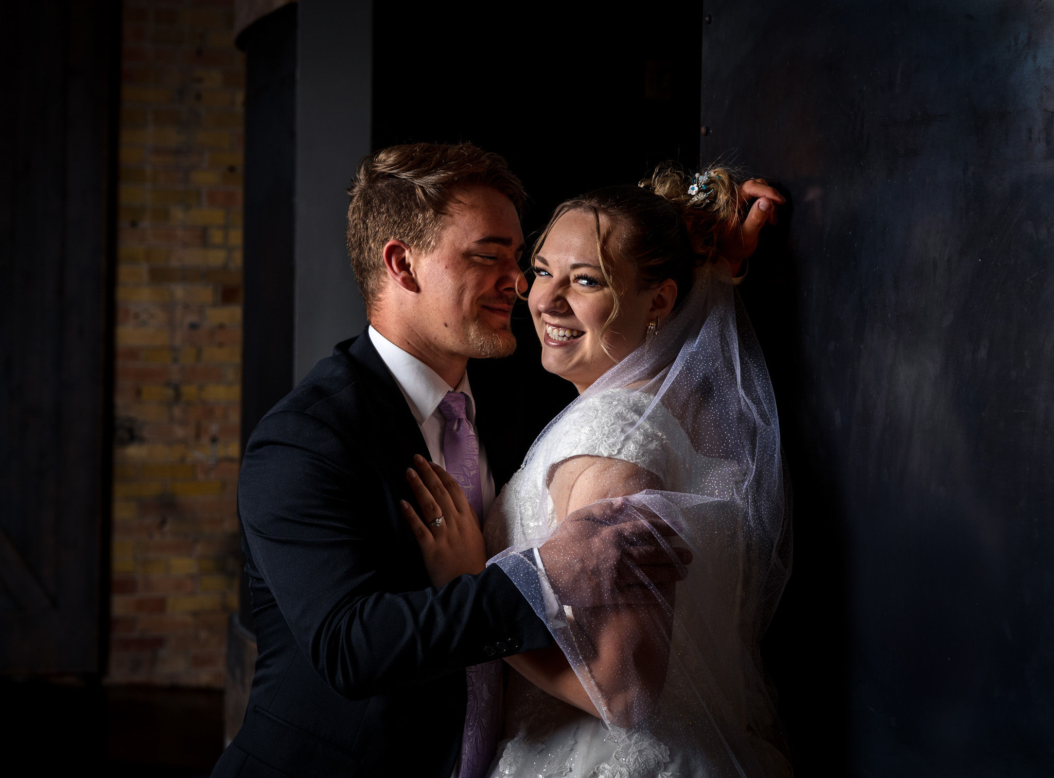 Bride and groom snuggly on metal wall.