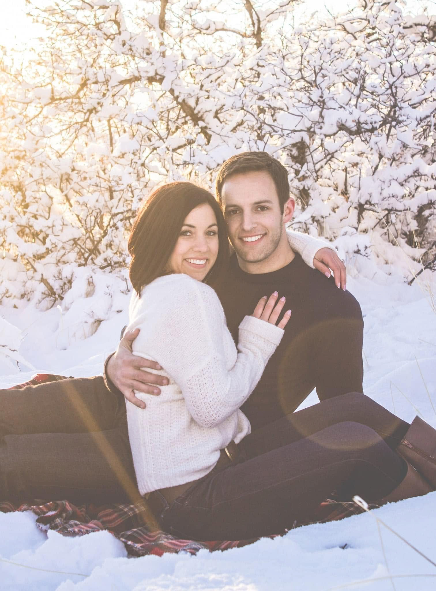 Couple cuddled up together in snow.