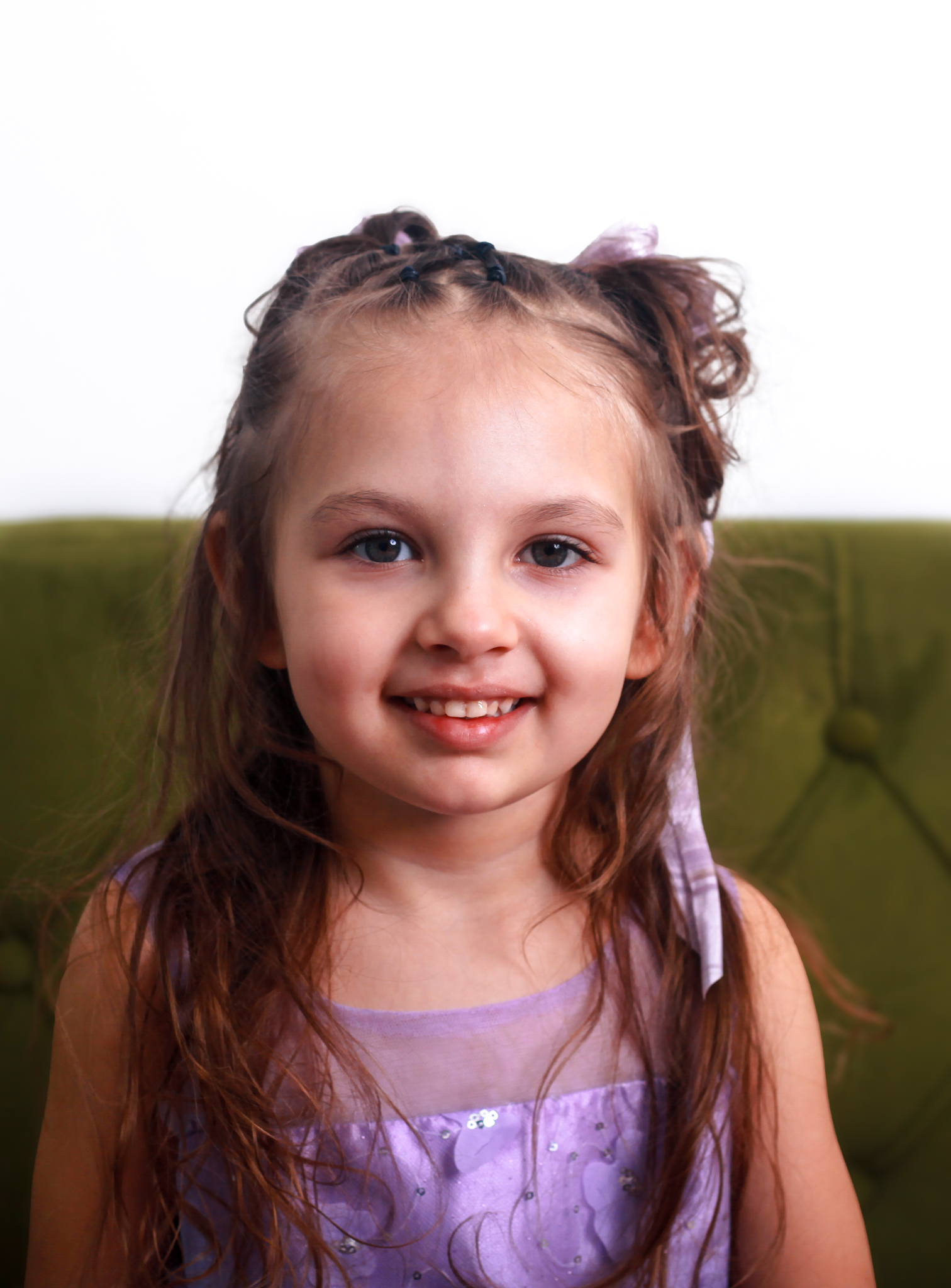 Little girl in purple dress on green couch.