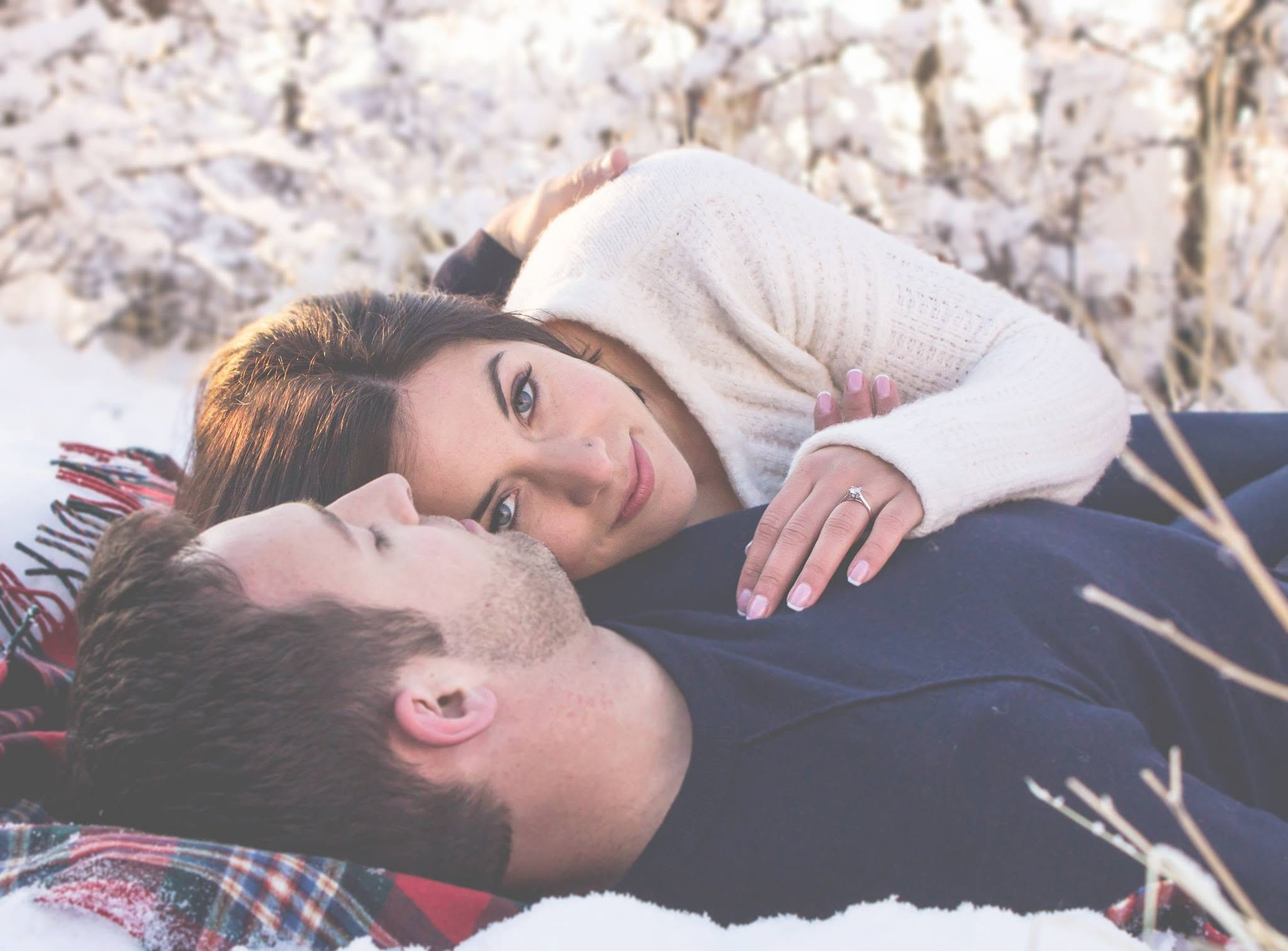Woman in snow laying on man's chest.