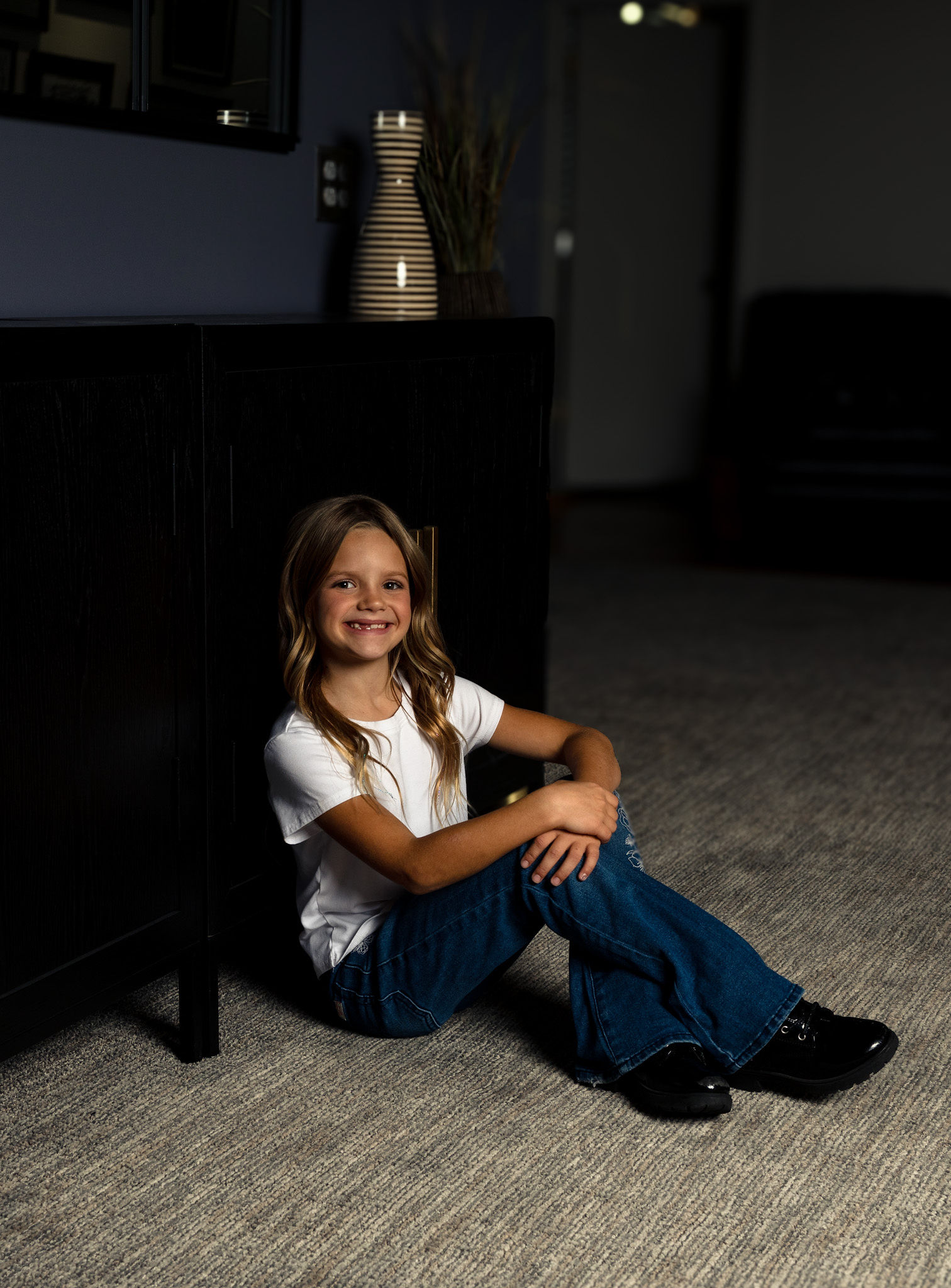 Little girl sitting against dresser.