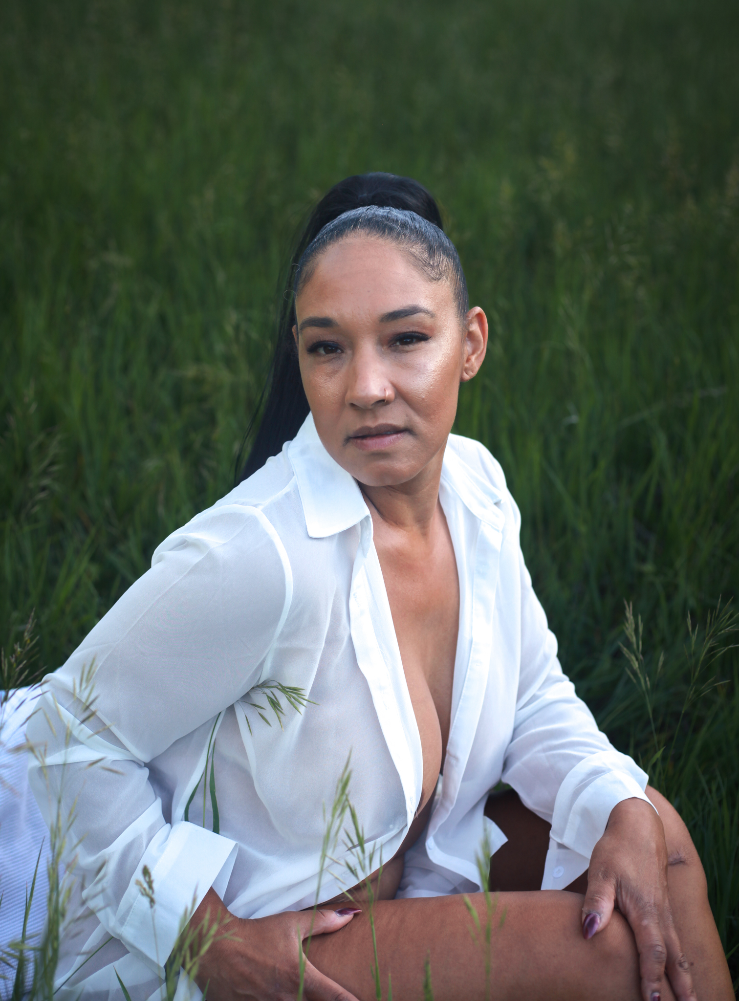 Woman sitting in field wearing button up shirt.