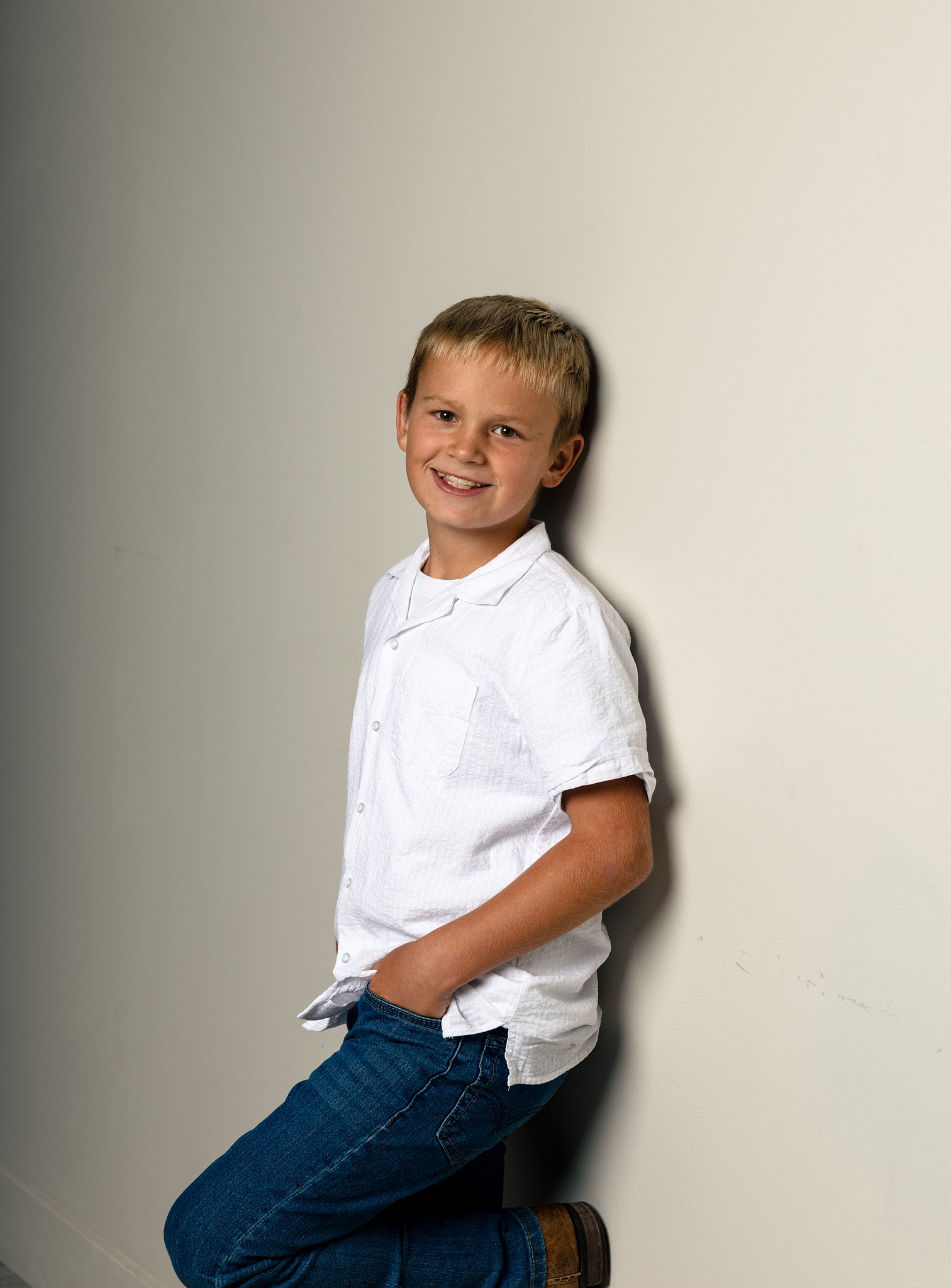 Little boy leaning against white wall.