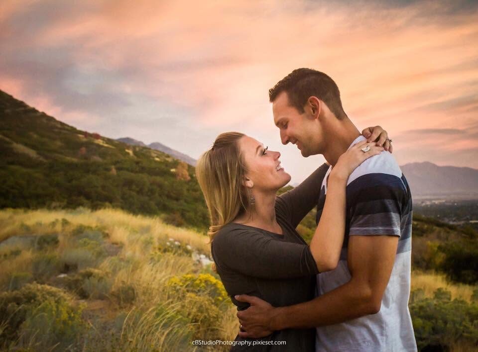 Couple embracing on a grassy hillside at sunset