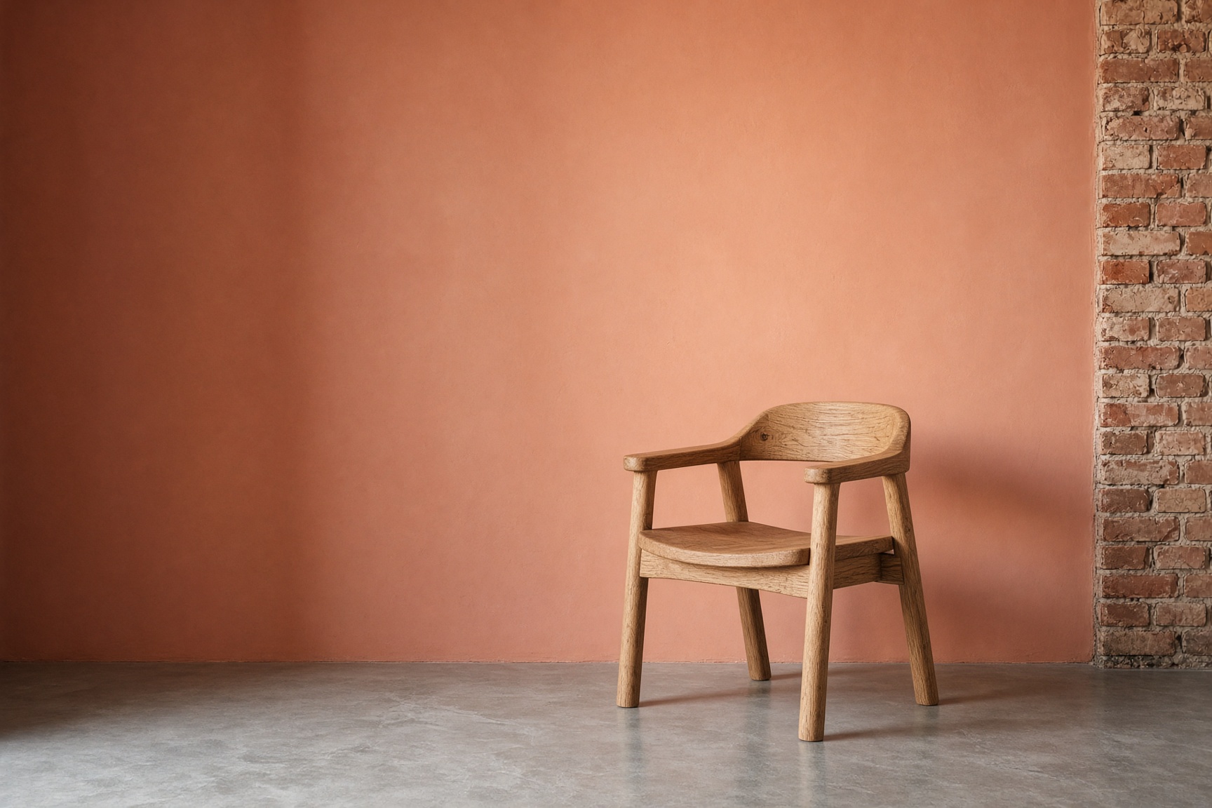 Warm terracotta clay painted wall used as a backdrop, sculptural oak chair off-center, soft light gradient.